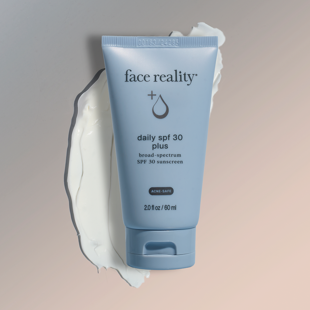 Tube of face reality daily SPF 30 plus sunscreen laying flat against white swatch on a gray-beige gradient background