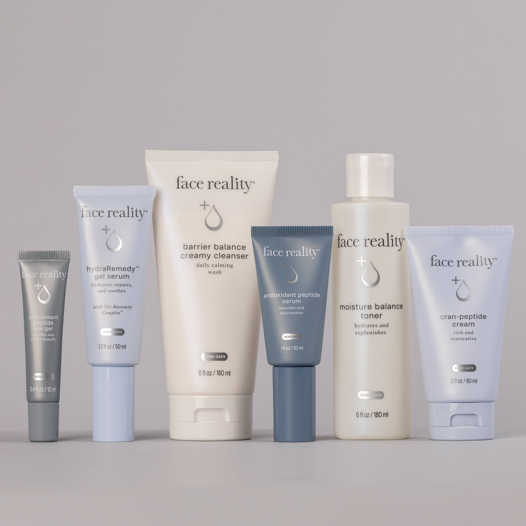 Face Reality Deluxe Age Defense Kit including 6 products: Antioxidant Peptide Eye Gel, hydraRemedy™ Gel Serum, Barrier Balance Creamy Cleanser, Antioxidant Peptide Serum, Moisture Balance Toner, and Cran-Peptide Cream (left to right) against light background