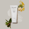 Tube of Face Reality antioxidant scrub with flowers and leaves on a light background