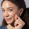 Model applying a single Face Reality invisiClear hydrocolloid spot patch on their cheek against a light background